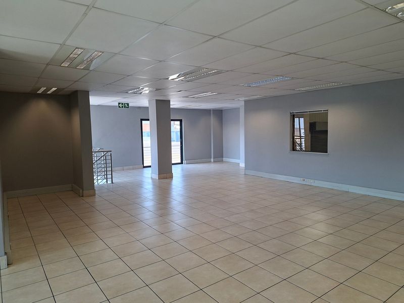 Spacious, open-plan industrial office area featuring neutral grey walls, ceramic tiled flooring, and a suspended ceiling with recessed lighting.