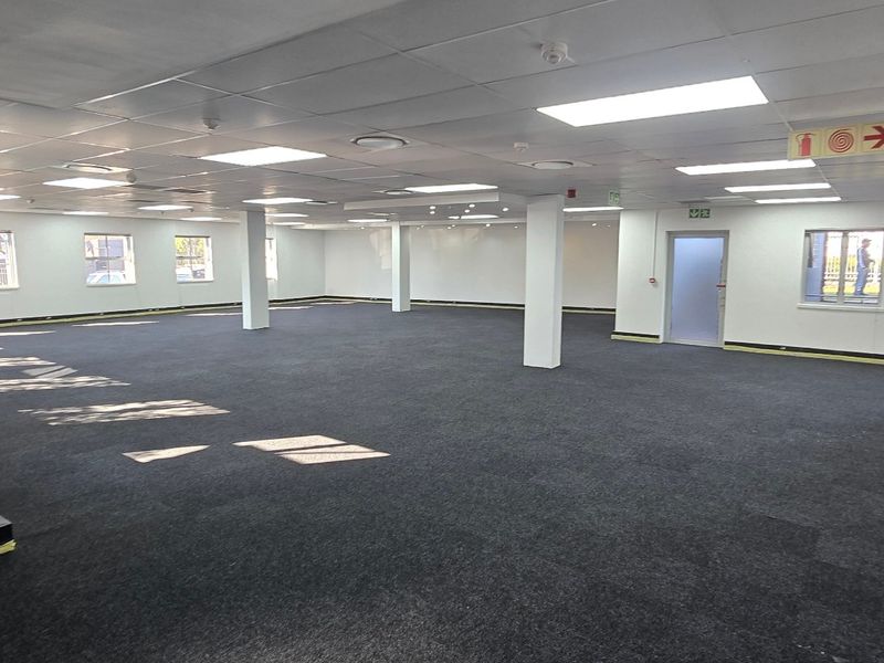A spacious, open-plan commercial office area featuring a suspended ceiling, recessed lighting, and dark carpet tiles, ready for custom fit-out.