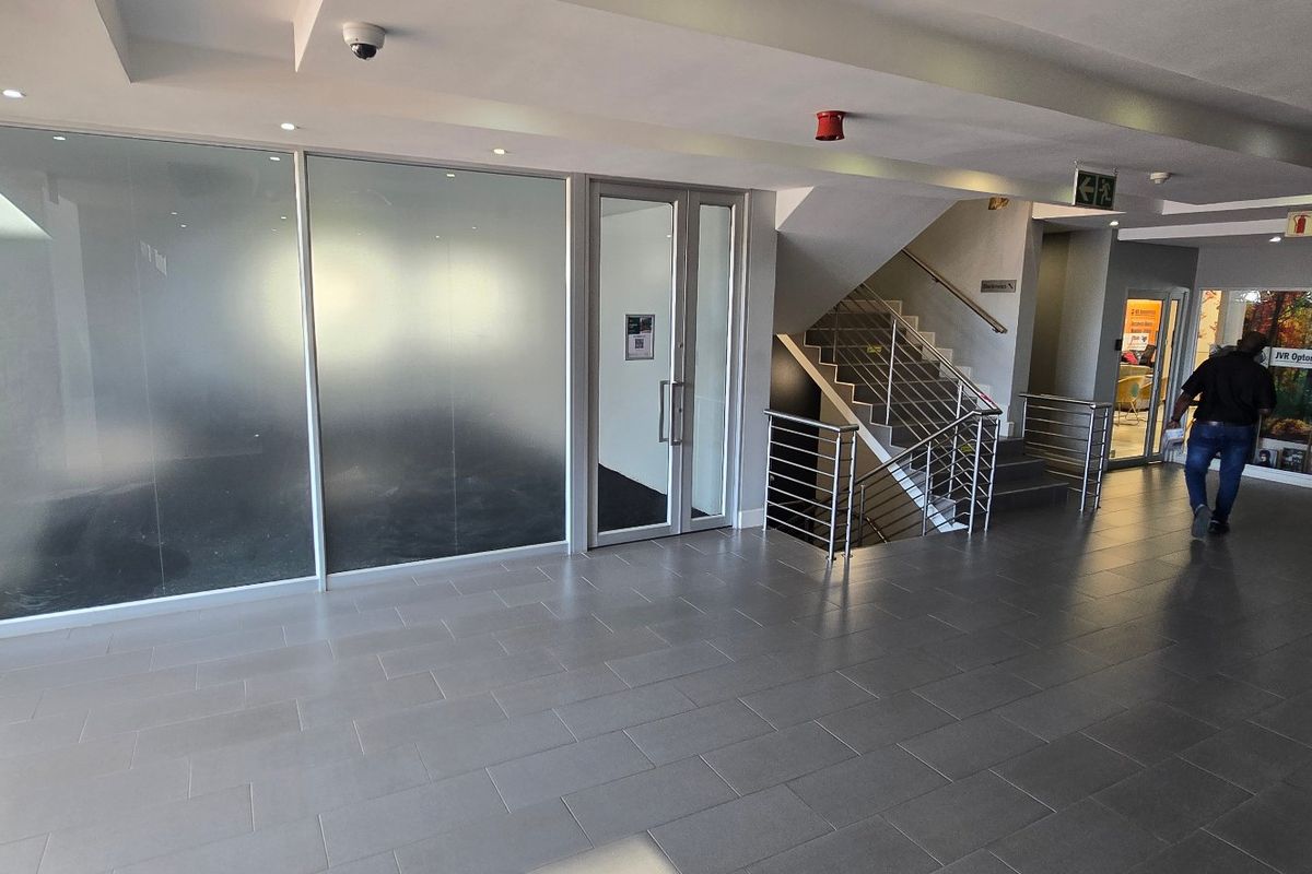 Modern commercial building entrance lobby featuring a stone feature wall, tiled flooring, frosted glass office partitions, and a stainless steel staircase.