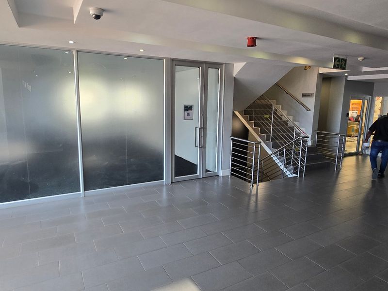 Modern commercial building entrance lobby featuring a stone feature wall, tiled flooring, frosted glass office partitions, and a stainless steel staircase.