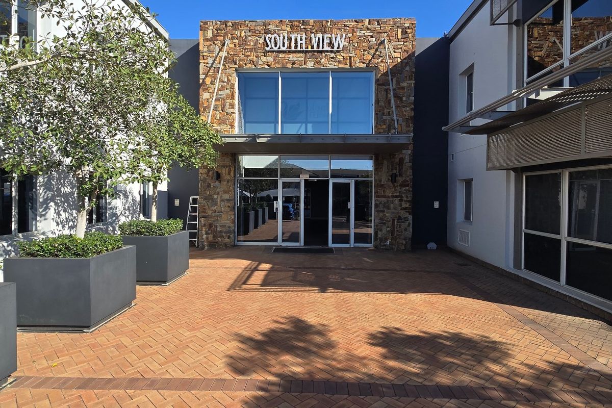 Modern commercial building entrance featuring a stone-clad facade, large glass windows, and a well-maintained brick-paved courtyard area.
