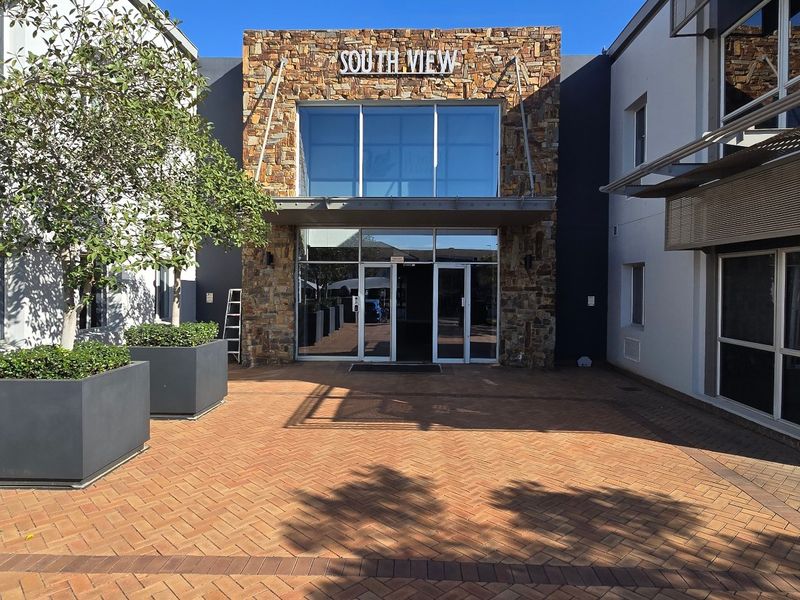 Modern commercial building entrance featuring a stone-clad facade, large glass windows, and a well-maintained brick-paved courtyard area.
