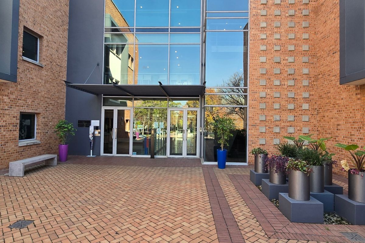 Modern commercial building entrance featuring a brick facade, expansive glass curtain wall, and a paved courtyard area.