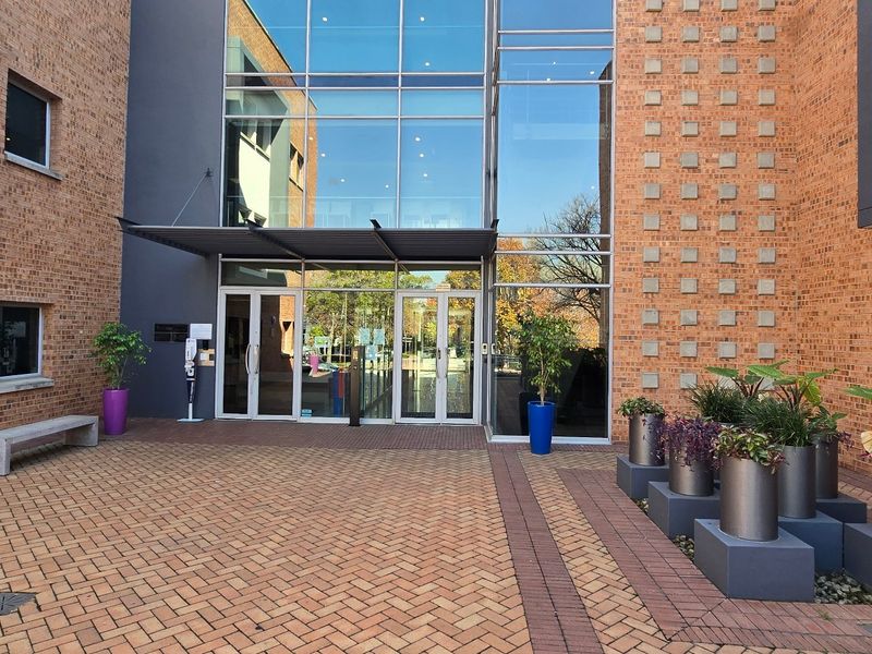 Modern commercial building entrance featuring a brick facade, expansive glass curtain wall, and a paved courtyard area.