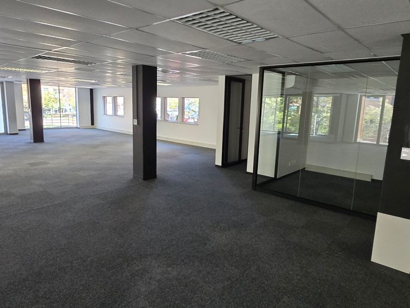 Spacious open-plan commercial office area featuring carpeted flooring, suspended ceilings, and modern glass-partitioned private offices with ample natural light.