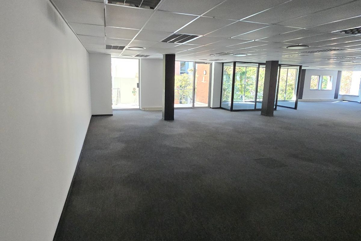 Spacious open-plan commercial office area featuring suspended ceilings, recessed lighting, structural columns, and large windows providing ample natural light.