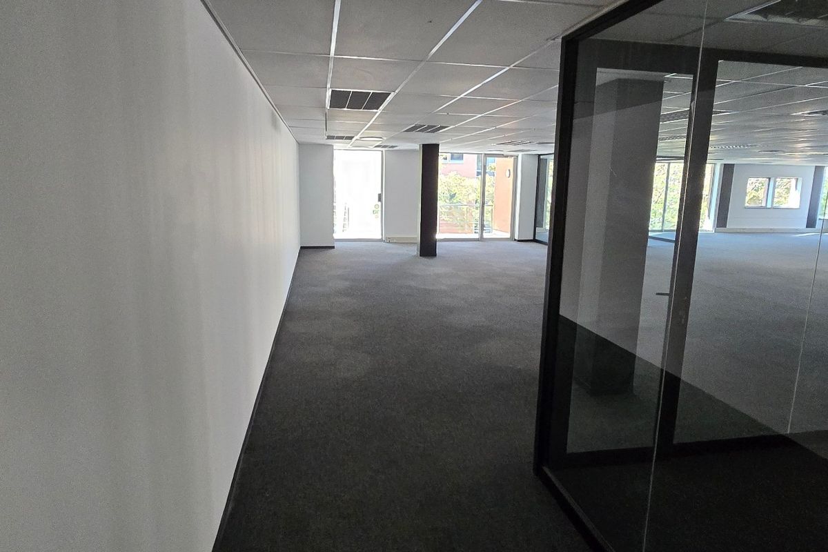 An open-plan commercial office space featuring carpeted flooring, a suspended ceiling, and modern glass partitioning, offering a clean and professional work environment.