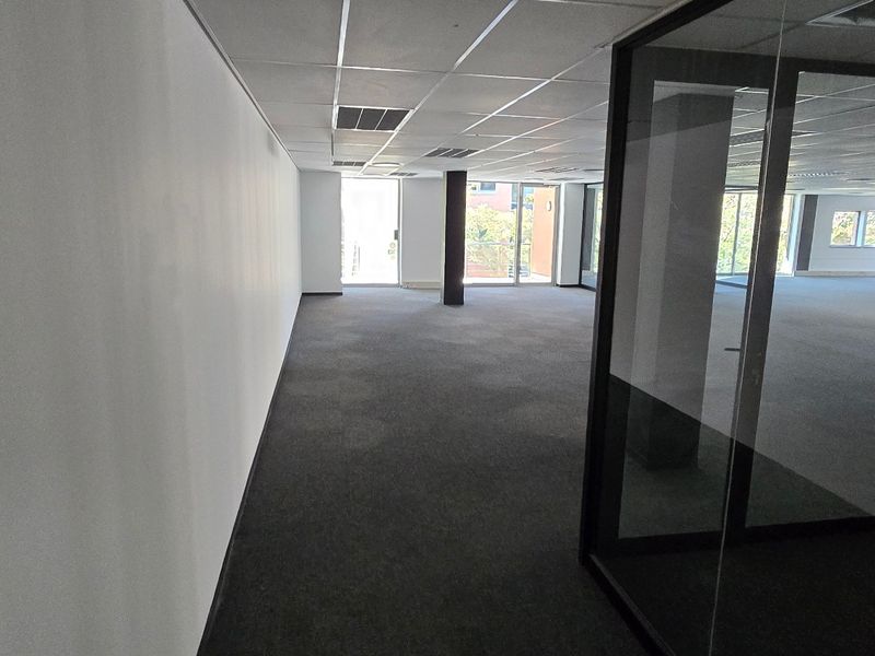 An open-plan commercial office space featuring carpeted flooring, a suspended ceiling, and modern glass partitioning, offering a clean and professional work environment.