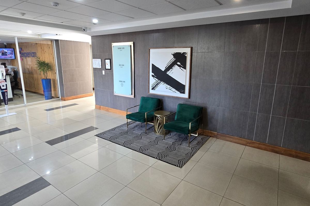 A modern commercial building entrance lobby featuring polished tiled floors, a suspended ceiling, and a glass-partitioned office area.