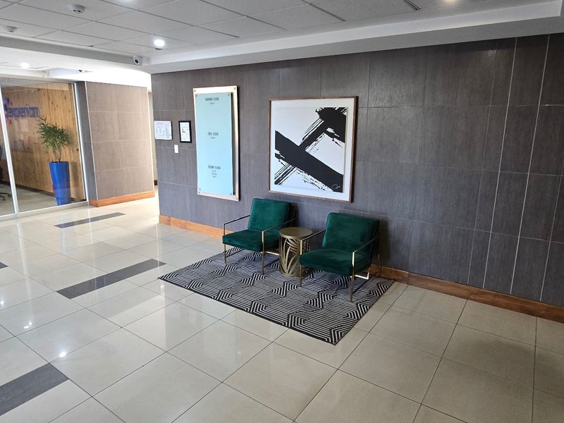 A modern commercial building entrance lobby featuring polished tiled floors, a suspended ceiling, and a glass-partitioned office area.