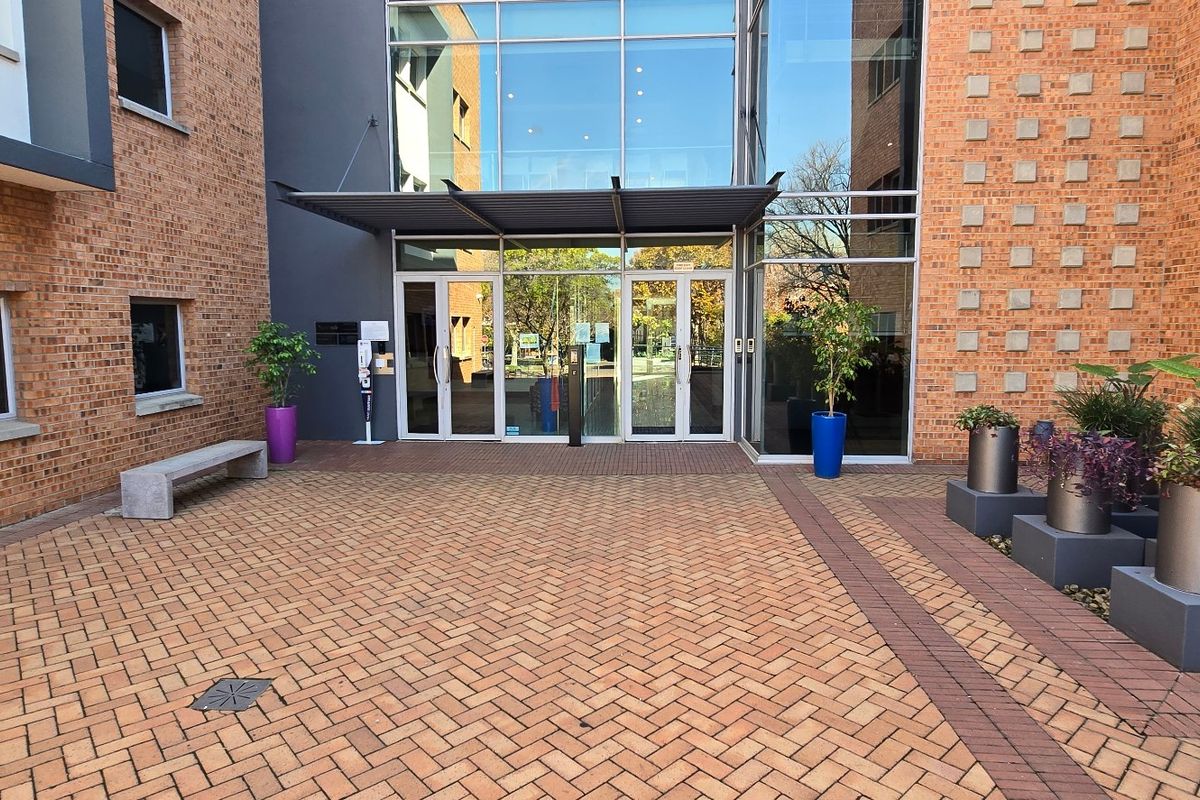 A modern commercial building entrance featuring a brick facade, glass curtain wall, and a paved courtyard area.