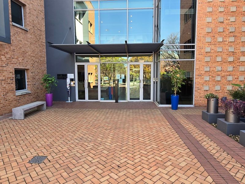 A modern commercial building entrance featuring a brick facade, glass curtain wall, and a paved courtyard area.