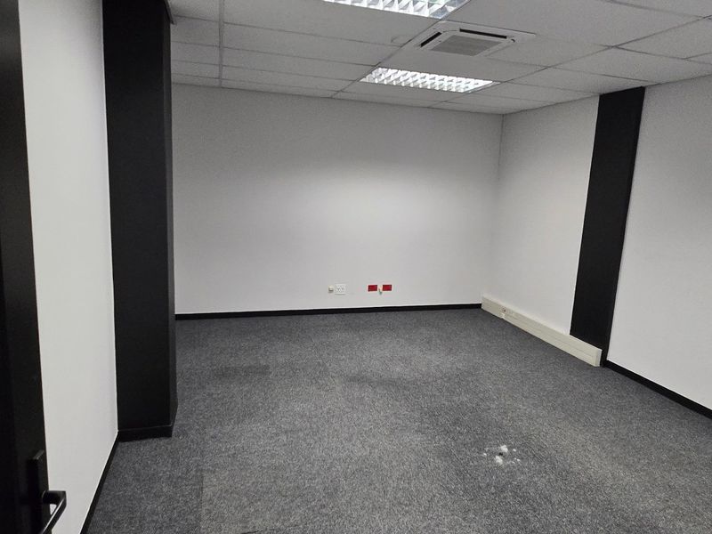 An empty commercial office space featuring grey carpet flooring, suspended ceiling with recessed lighting, and integrated ducted air conditioning.