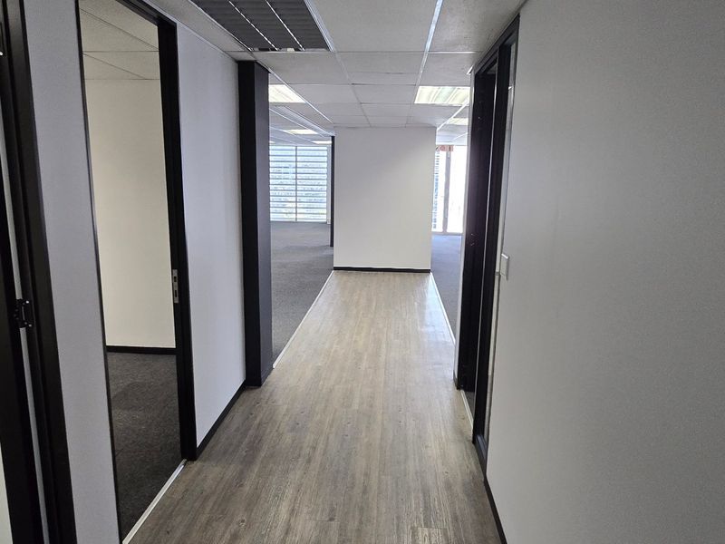 A clean, modern commercial office hallway featuring wood-look laminate flooring, suspended ceilings, and access to multiple partitioned office spaces.