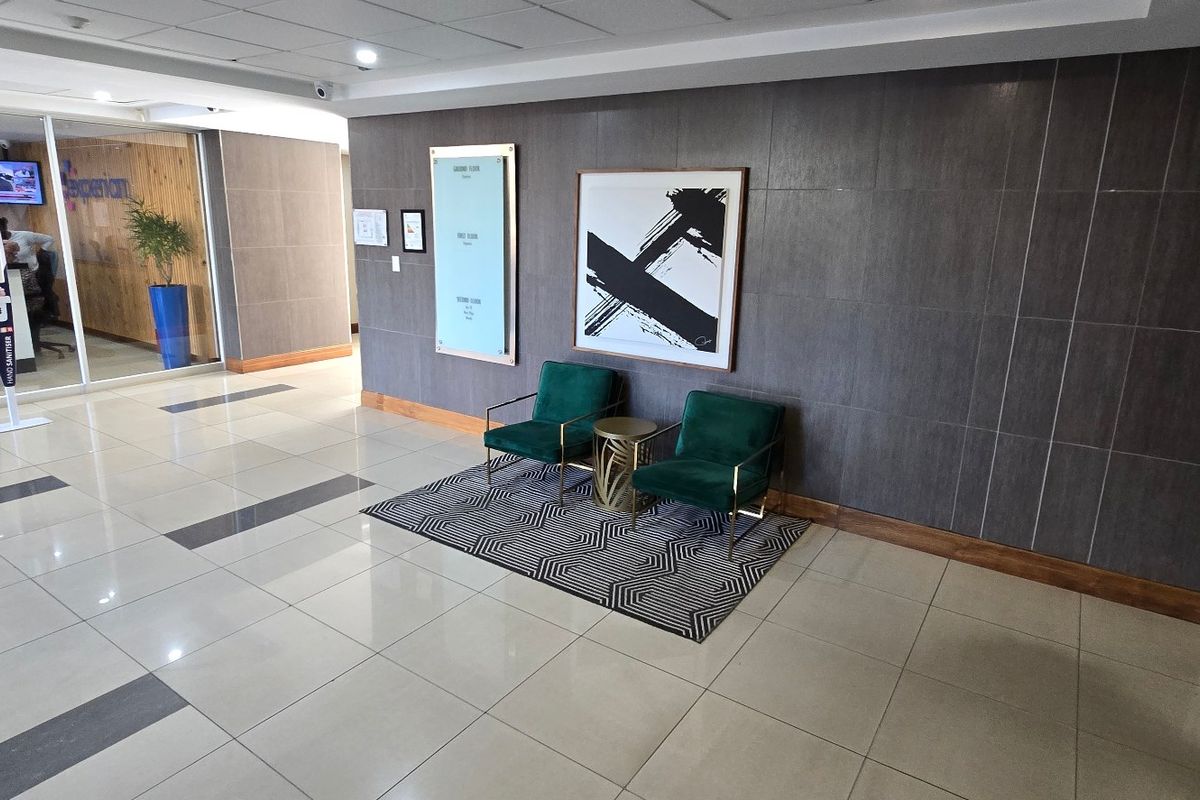 A modern commercial building entrance lobby featuring polished tiled flooring, dark feature wall paneling, and a glass-partitioned office area.