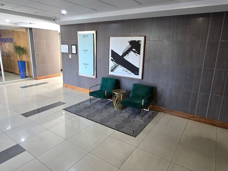A modern commercial building entrance lobby featuring polished tiled flooring, dark feature wall paneling, and a glass-partitioned office area.