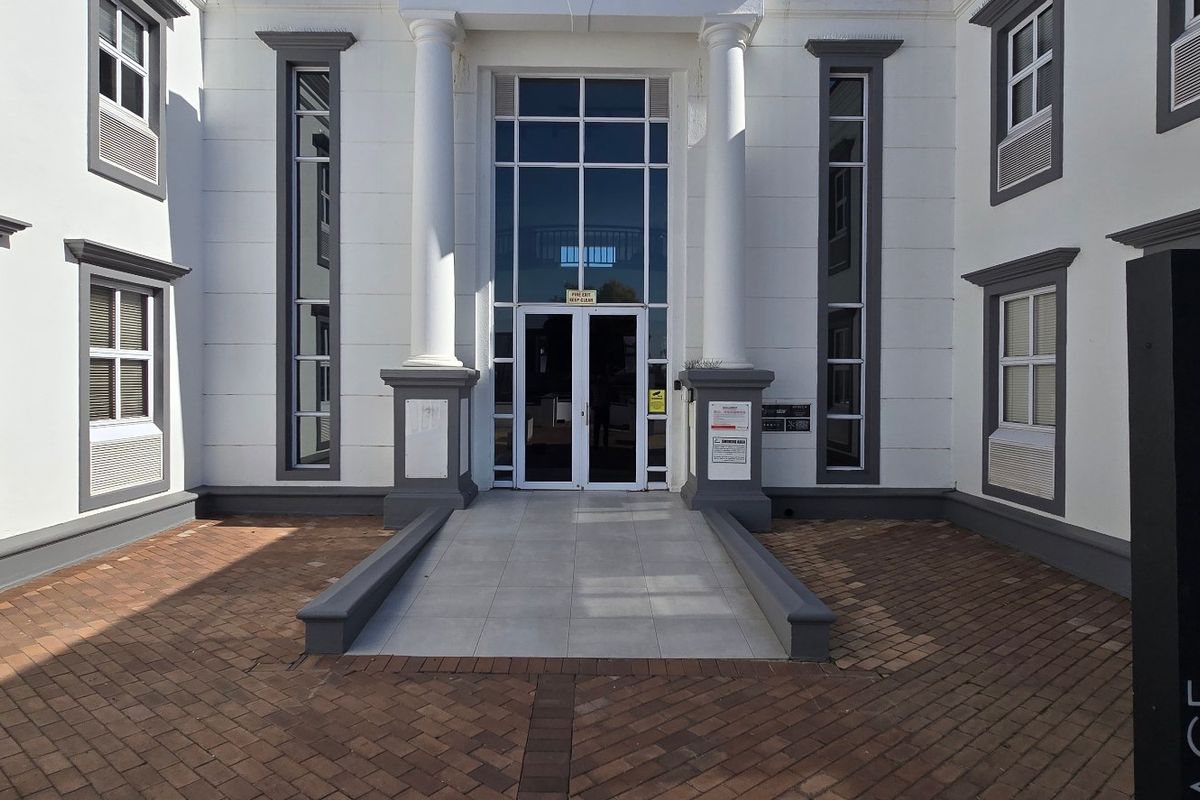 Front entrance of a commercial building featuring a paved courtyard, classical columns, and a glass-fronted entryway with professional signage.