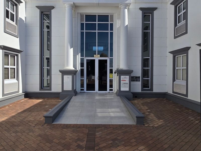 Front entrance of a commercial building featuring a paved courtyard, classical columns, and a glass-fronted entryway with professional signage.
