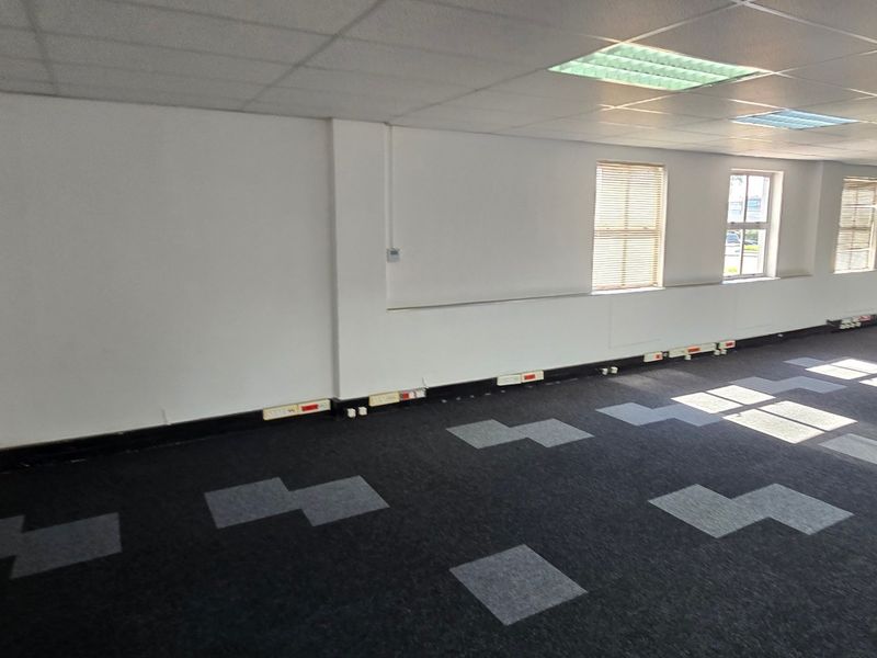 A spacious, empty open-plan office area featuring carpet tiles, suspended ceilings with recessed lighting, and perimeter trunking for electrical and data connectivity.