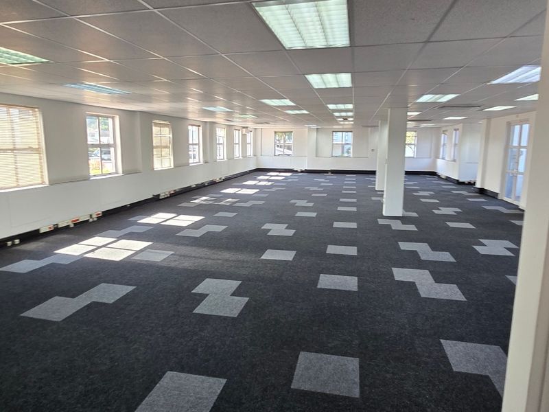 Spacious open-plan commercial office area featuring suspended ceilings, recessed lighting, perimeter trunking, and modern patterned carpet tiles.