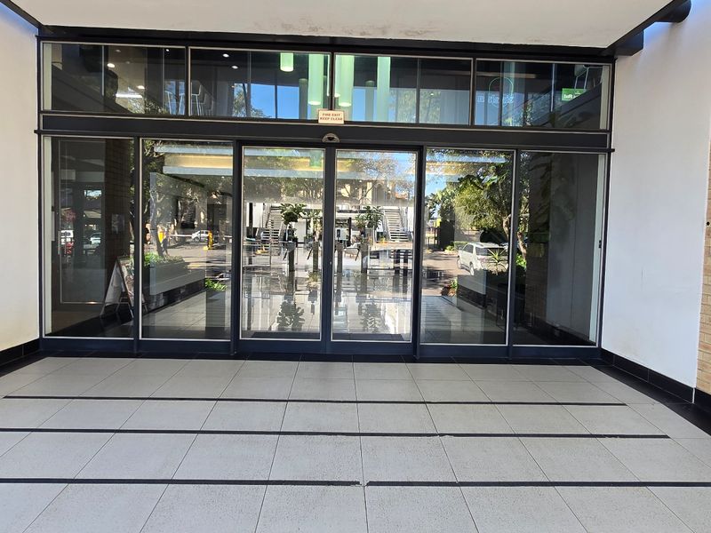 Modern commercial building entrance featuring automatic sliding glass doors, tiled flooring, and an exposed brick facade.