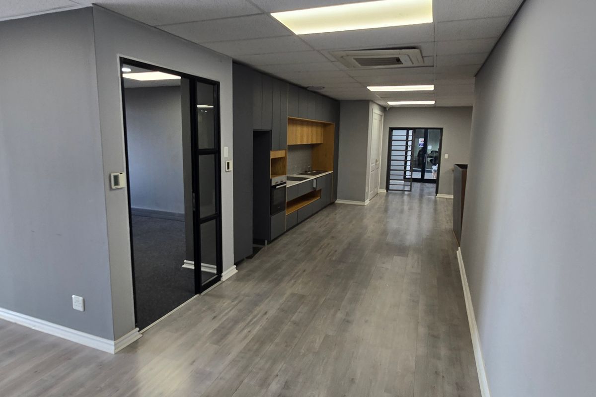 Modern commercial kitchenette featuring sleek grey cabinetry, integrated oven, sink, and durable laminate flooring within a clean, open-plan office environment.