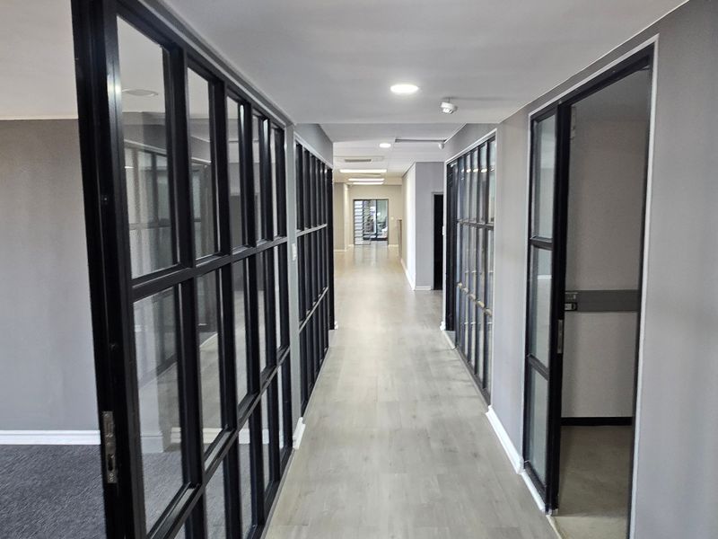 Modern commercial hallway featuring black steel-framed glass partitions, recessed lighting, and durable laminate flooring, providing a clean and professional office aesthetic.