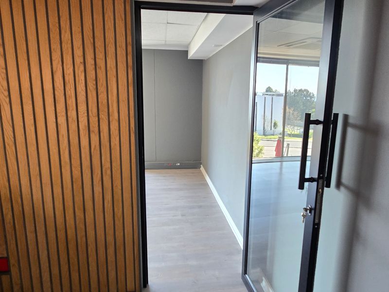 A modern, empty office space featuring contemporary timber slat wall paneling, laminate flooring, and a glass entrance door with a view of the exterior.