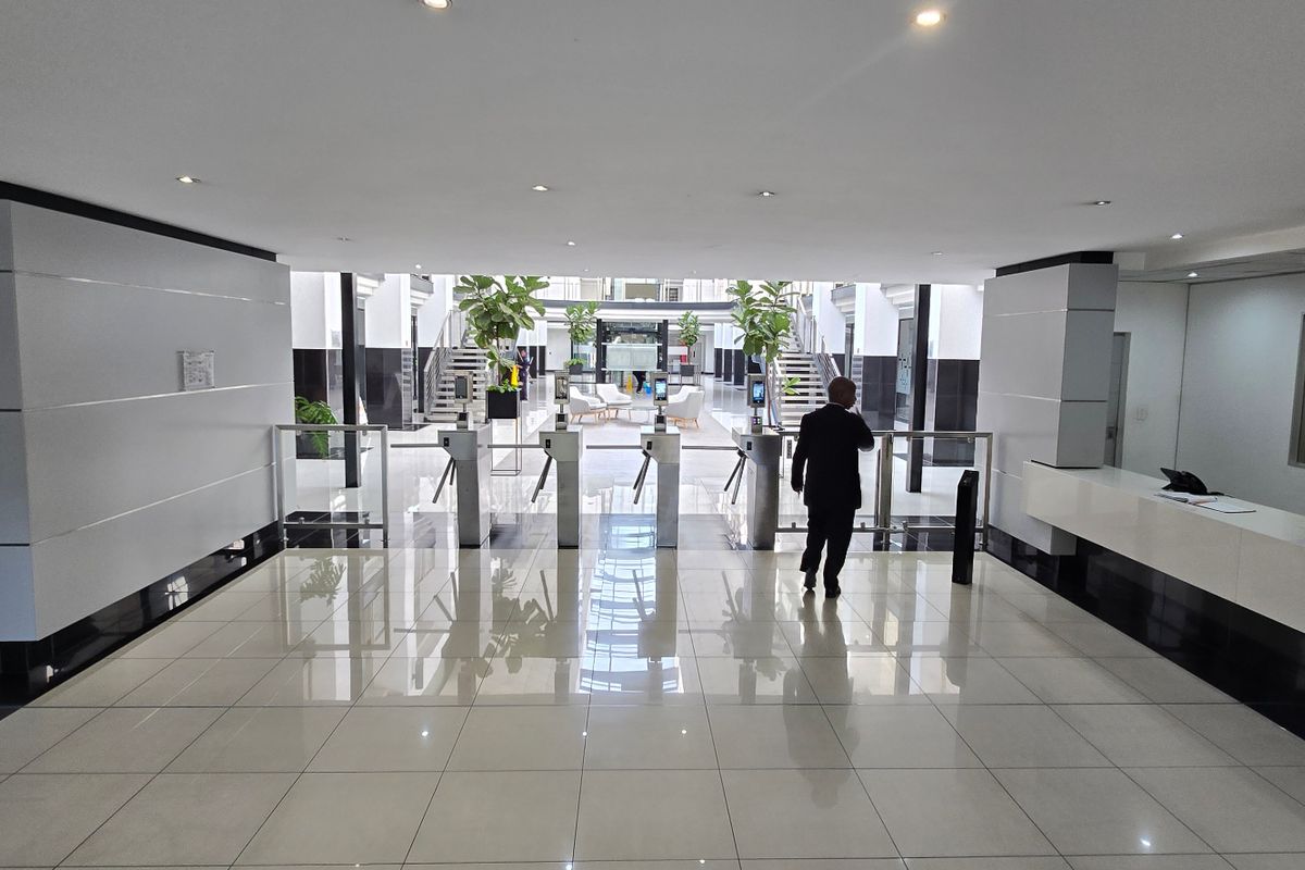 Modern commercial building entrance lobby featuring a reception desk, security turnstiles, and polished tiled flooring with recessed lighting.