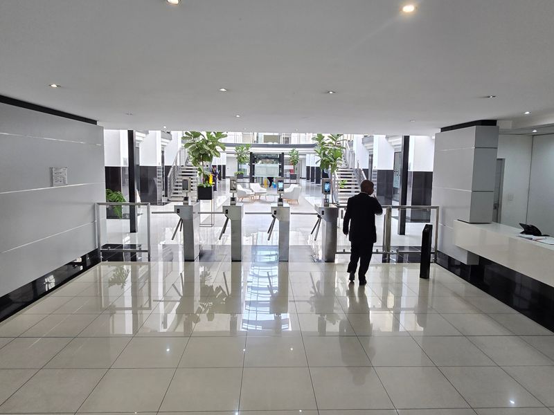 Modern commercial building entrance lobby featuring a reception desk, security turnstiles, and polished tiled flooring with recessed lighting.