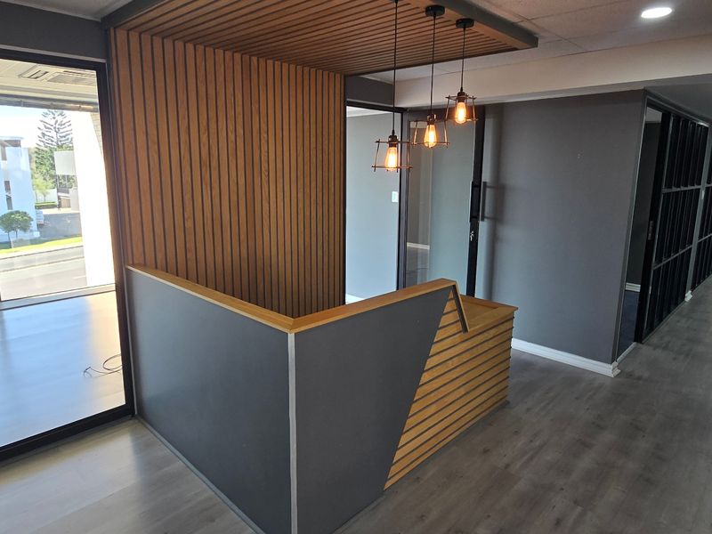 Modern commercial office entrance featuring a custom built-in reception desk, slatted timber accent wall, and sleek laminate flooring with glass partition detailing.