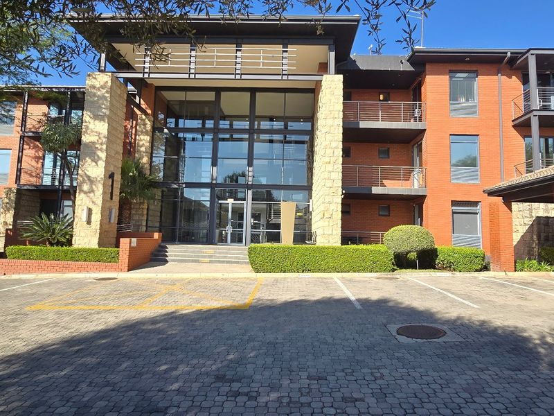 Modern commercial office building featuring a prominent glass entrance, brick and stone facade, and dedicated paved parking area.