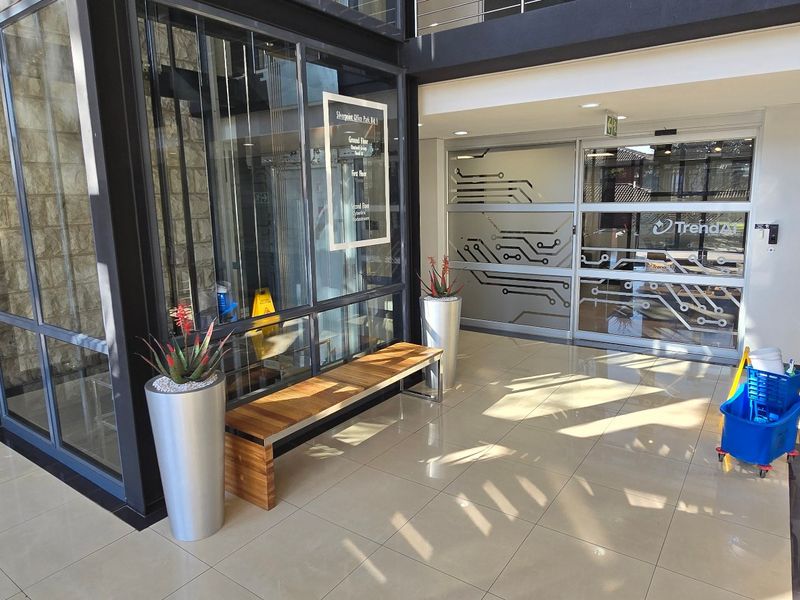 Modern commercial building entrance lobby featuring a glass elevator, stone accent wall, tiled floors, and automatic sliding glass doors with decorative circuit board patterns.