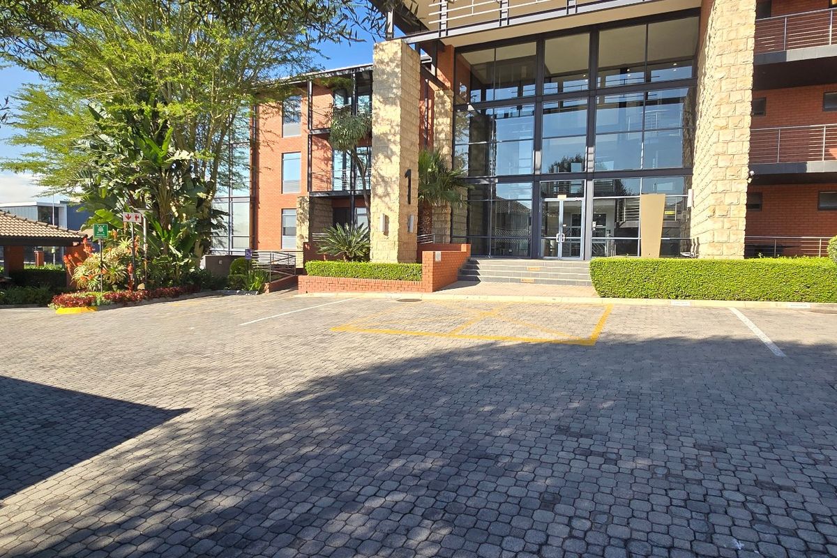 Front exterior view of a modern commercial building featuring stone and brick facade, large glass entrance, and paved parking area with covered bays.