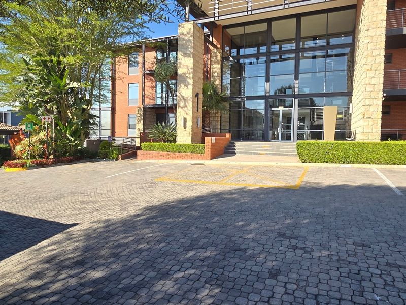 Front exterior view of a modern commercial building featuring stone and brick facade, large glass entrance, and paved parking area with covered bays.