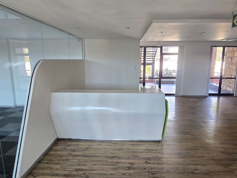 Modern commercial office space featuring a reception desk, glass partitions, laminate flooring, and carpeted areas with integrated emergency exit signage.