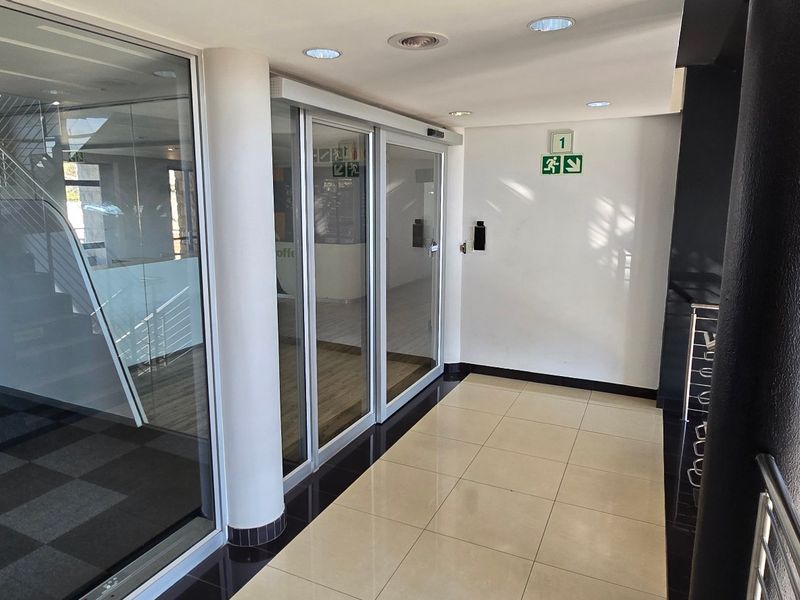 A clean, modern commercial entrance lobby featuring tiled flooring, glass sliding doors, and a staircase with metal railings.