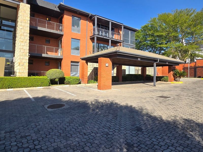 Front exterior view of a commercial office building featuring a brick facade, glass curtain wall, and a covered porte-cochere entrance with paved parking.
