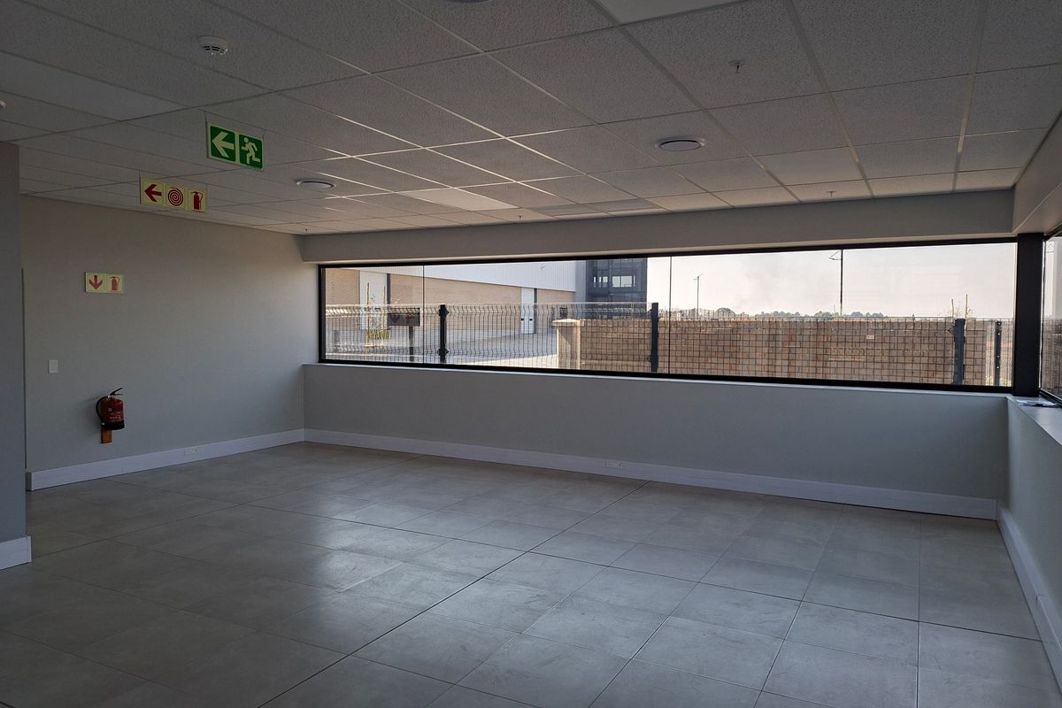 A bright, open-plan office space featuring modern tiled flooring, a suspended ceiling with recessed lighting, and a large window providing natural light.