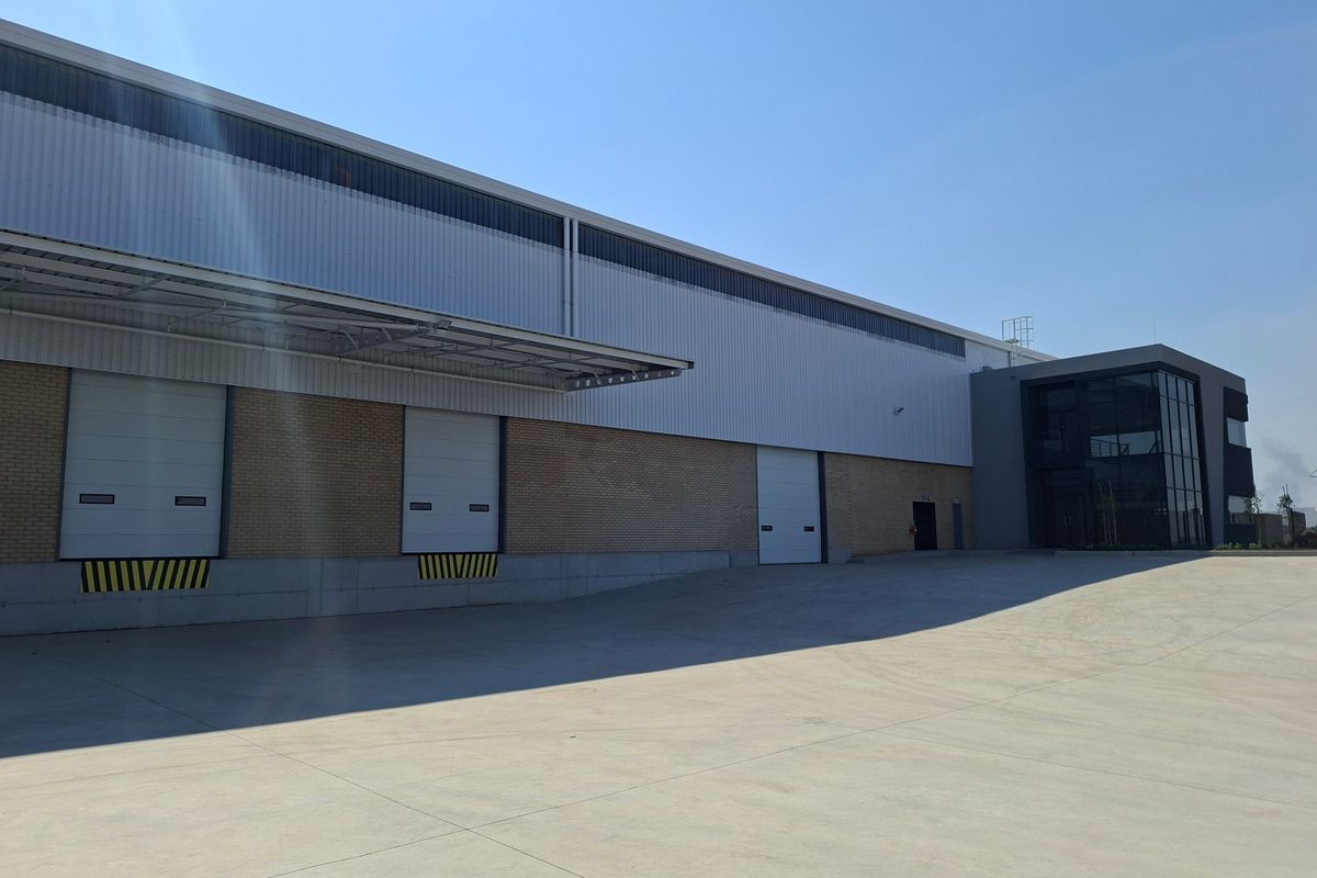 Modern industrial warehouse exterior featuring multiple roller shutter loading doors, a spacious concrete yard, and a contemporary glass-fronted office section.