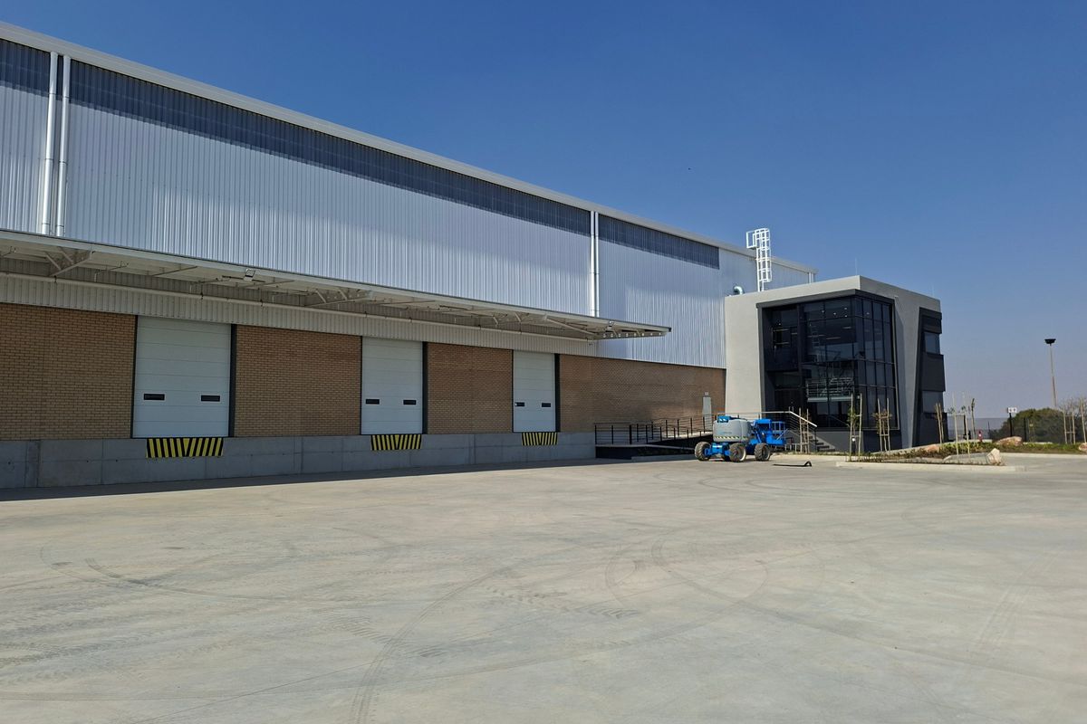 Modern industrial warehouse facility featuring multiple roller shutter loading doors, a spacious concrete yard, and a contemporary glass-fronted office section.