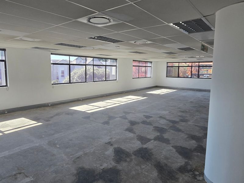 Spacious open-plan office area featuring large windows, a suspended ceiling with recessed lighting, and an exposed concrete floor ready for new flooring installation.