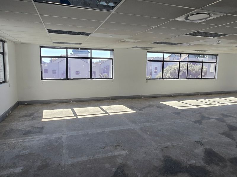Spacious, vacant commercial office area featuring large aluminium windows, suspended ceilings with recessed lighting, and an unfinished concrete floor ready for custom flooring installation.