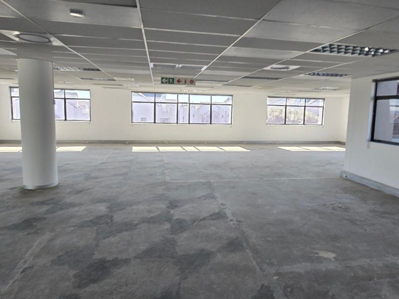An open-plan commercial office space featuring a suspended ceiling, structural columns, and large windows providing ample natural light.