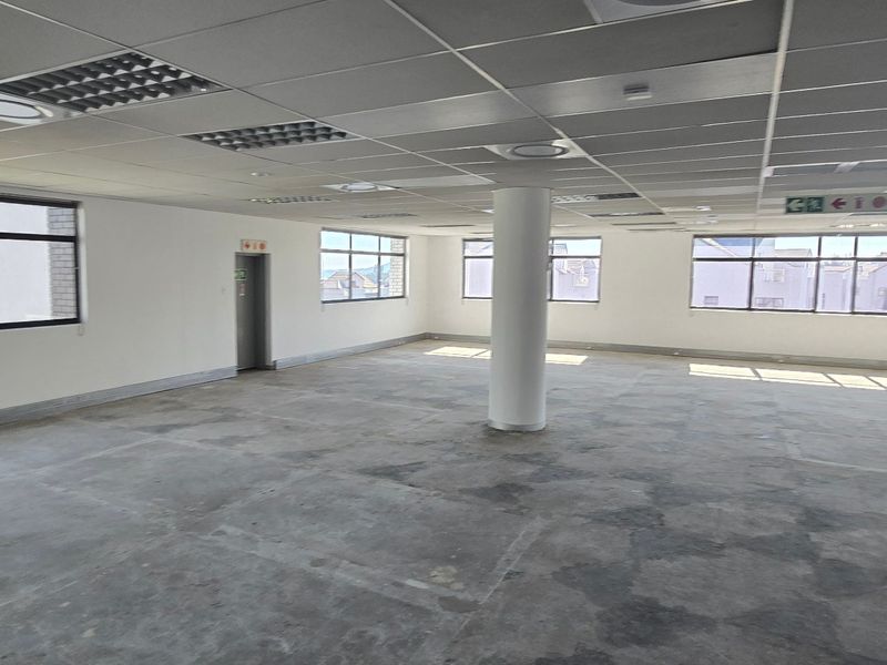 A spacious, open-plan commercial office area featuring a suspended ceiling, recessed lighting, and large windows providing ample natural light.