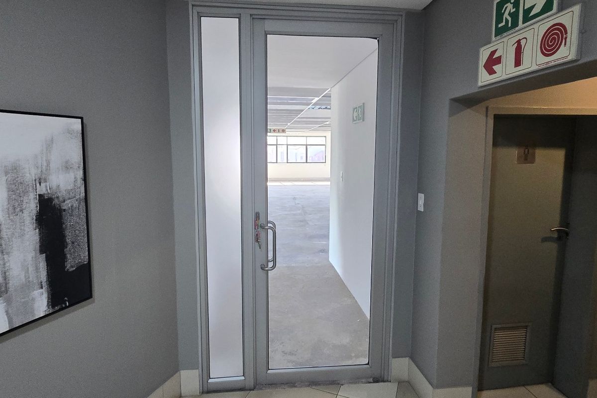 A clean commercial hallway featuring an aluminium framed glass door, fire safety signage, and neutral grey wall finishes.