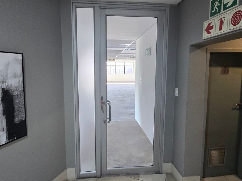 A clean commercial hallway featuring an aluminium framed glass door, fire safety signage, and neutral grey wall finishes.