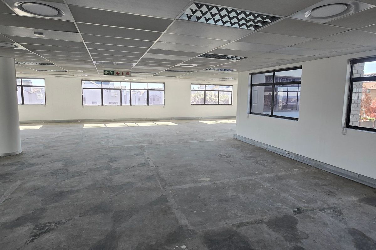 A spacious, open-plan commercial office area featuring a suspended ceiling, recessed lighting, and large windows providing ample natural light.