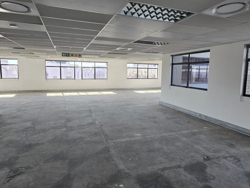 A spacious, open-plan commercial office area featuring a suspended ceiling, recessed lighting, and large windows providing ample natural light.