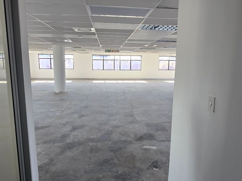 An expansive, open-plan commercial office space featuring a suspended ceiling, recessed lighting, and large windows providing ample natural light.